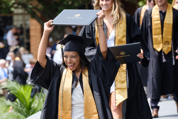 A graduate raises her diploma above her head at commencement 2022.