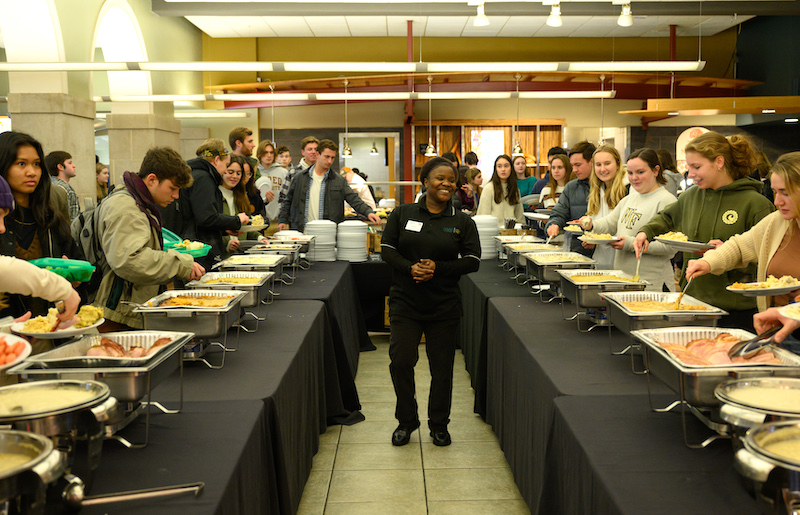 Wake Forest students go through the buffet line for Pitsgiving. In the middle of the tables of food, a Harvest Table employee smiles.